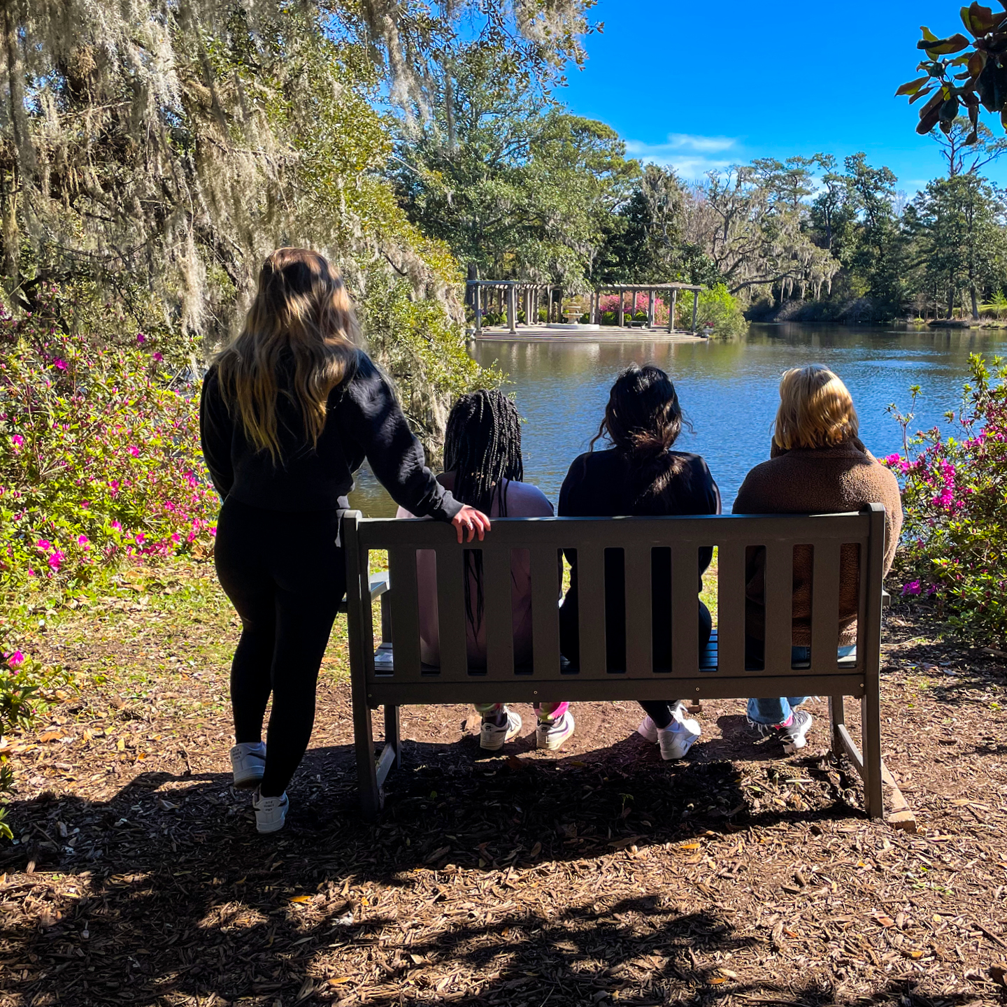 4 young women sitting on a bench looking at water