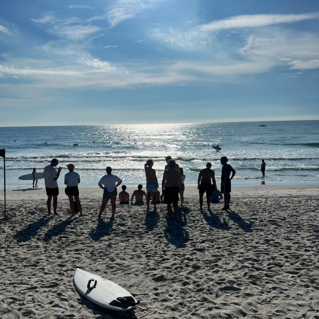 Group of guys on the beach with a surfboard looking at the horizon