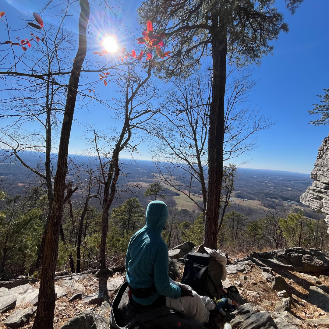 young adult sitting on a rock looking out over the landscape